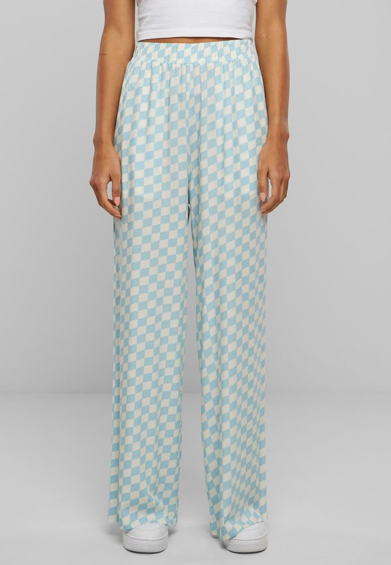 Pantalon à jambes larges avec un motif à damier bleu clair et blanc, porté avec des baskets blanches et un top blanc court.