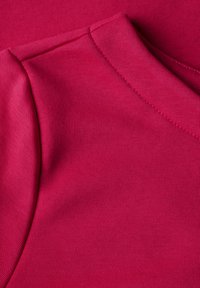 Upletený top s krátkým rukávem ve světlé růžové barvě, vyrobený z hladkého materiálu s jemným vzorem, který má klasický kulatý výstřih a ševové detaily.