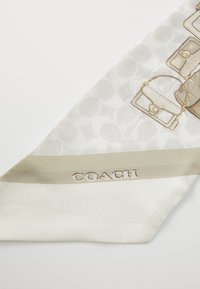 Hedvábný šátek s krémovým podkladem, na kterém jsou vzorované kabelky v světlé hnědé barvě. Logo "COACH" je reliéfně vyraženo na béžovém pruhu podél okraje.