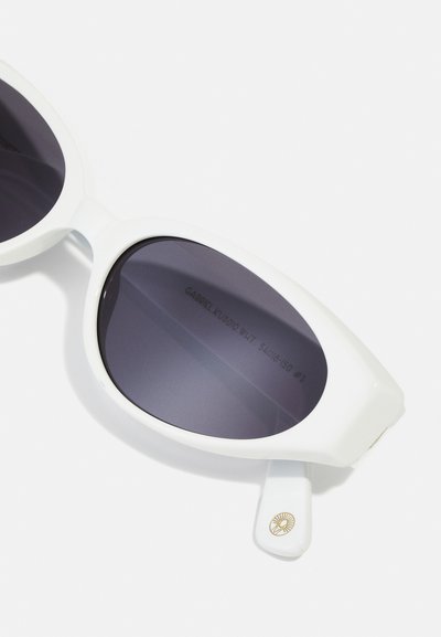 White oversized sunglasses with dark tinted lenses, rounded shape, and subtle gold branding detail on the temple. Textured frame finish.