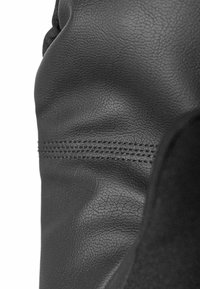 Schwarzes Lederdetail mit einer strukturierten Oberfläche und sichtbaren Stichen. Das Design ist glatt mit leichter Krümmung, die die Qualität des Materials hervorhebt.