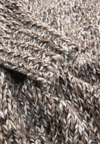 Gros plan sur un tissu tricoté épais marbré marron et blanc avec des bords de poignets côtelés visibles et un motif de points texturé.