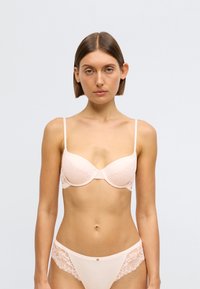 Στήθους χρώματος δέρματος στηθόδεσμος με δαντέλα, με ενσωματωμένη στηρίξη και ρυθμιζόμενους ιμάντες. Συμπληρώνεται από ταίριασμα σλιπ διακοσμημένο με δαντέλα.