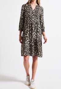 Klänning med leopardmönster i beige och svart, med v-ringning, trekvartslånga ärmar och en skräddad kjol. Bärs tillsammans med vita sneakers.