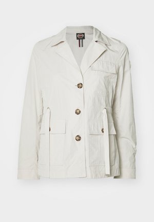 Világos bézs színű dzseki, könnyű anyagból készült. Galléros nyakkal, elülső gombokkal, két zsebből és állítható derékrésszel rendelkezik, amely húzózsinórral állítható.