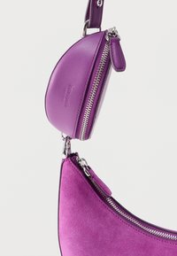 Μωβ δερμάτινη και σουέτ τσάντα χειρός με καμπυλωτό σχέδιο, που διαθέτει ασημένια μεταλλικά στοιχεία και αποσπώμενο τσαντάκι με φερμουάρ.