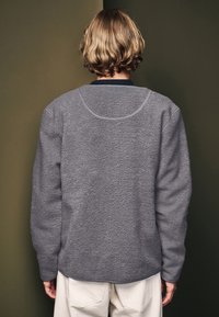 Sweatshirt en polaire gris texturé avec manches longues, encolure arrondie et ourlet incurvé. La vue arrière montre un matériau doux et un design sans embellissement.
