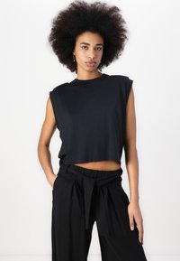 Black cropped t-shirt with short sleeves, featuring a crew neck and soft texture. Paired with high-waisted black trousers with a tied waistband.