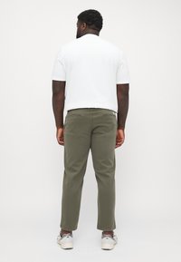 Camiseta blanca de manga corta y chinos en color verde oliva, con corte recto. Los pantalones tienen dos bolsillos traseros y se combinan con zapatos de color claro.