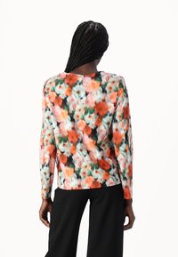 Blomstrete langermet topp med et flerfarget mønster i oransje, rosa og grønn mot en svart bakgrunn; rund hals og avslappet passform.