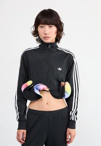 Veste de sport noire cropped avec zip et col haut, ornée de détails colorés en arc-en-ciel au niveau de l'ourlet, assortie à un jogging noir.