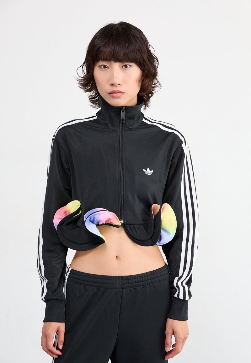 Veste de sport noire cropped avec zip et col haut, ornée de détails colorés en arc-en-ciel au niveau de l'ourlet, assortie à un jogging noir.