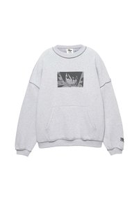 Grå sweatshirt med rund hals, oversized pasform, frontlomme og en sort grafisk patch med en karakter over lommen.