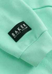 Sweatshirtstof in muntgroen met geribbelde manchetten. Voorzien van een zwart geweven label met de tekst "BAKER" en "by TED BAKER" in witte letters.