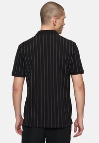 Svart randig polo skjorta med korta ärmar, klassisk krage och vertikala vita ränder. Tygets struktur verkar mjuk och bekväm.
