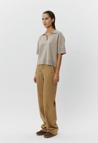 Svetlohnedá, trištvrťová polokošeľa s V-výstrihom a voľným strihom, skombinovaná s béžovými širokými nohavicami a tmavohnedou obuvou. Jednoduchý dizajn.