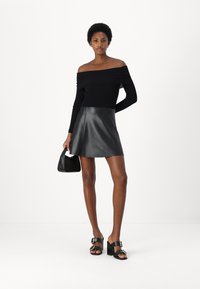 Top nero scoperto sulle spalle con maniche lunghe, abbinato a una mini gonna in pelle nera svasata e sandali neri con tacchi grandi. Piccola borsa nera.