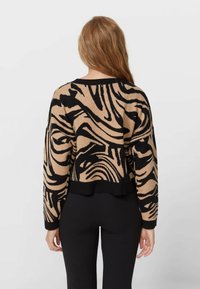 Beżowy i czarny sweter w paski zebry, wykonany na drutach, z krótkim fasonem, długimi rękawami i okrągłym dekoltem, z prążkowanym wykończeniem.