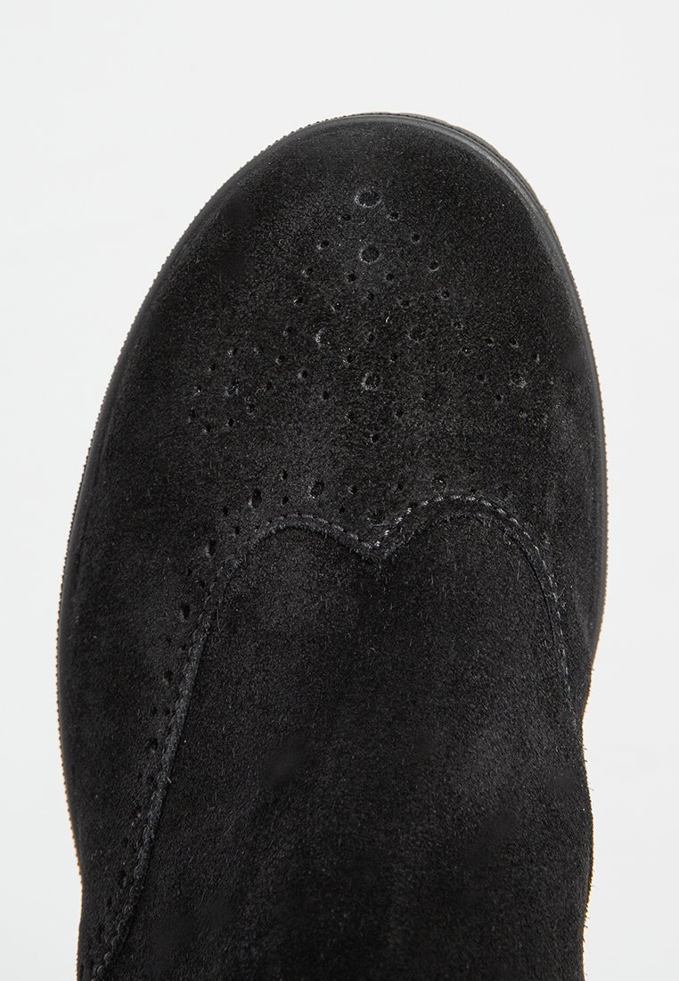Tige de chaussure en daim noir avec des détails perforés, des accents de couture courbés et une finition texturée. Forme de orteil ovale, bords cousus et semelles lisses.