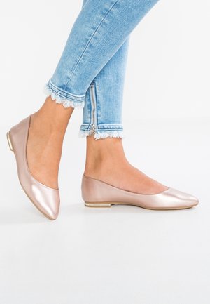 Ballerines en cuir lisse métallisé or rose avec un bout arrondi et un petit talon orné d'un accent doré. Portées avec un jean bleu clair effiloché.