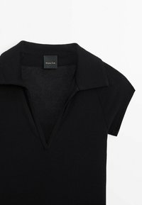 Haut en maille noir à manches courtes avec un col en V profond et un large col, avec une petite étiquette rectangulaire de la marque au niveau de l'encolure.
