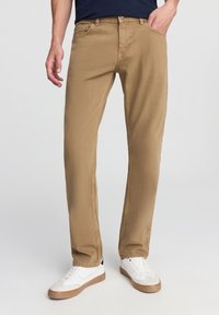 Chinos in cotone beige con una vestibilità a gamba dritta, dotati di tasche laterali e posteriori, abbinati a sneakers bianche. Design semplice, dettagli minimi.
