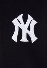 Sort stof prydes af et fremtrædende broderet hvidt "NY" logo, der fremviser et dristigt, stiliseret design med markante kurver og skarpe kanter.
