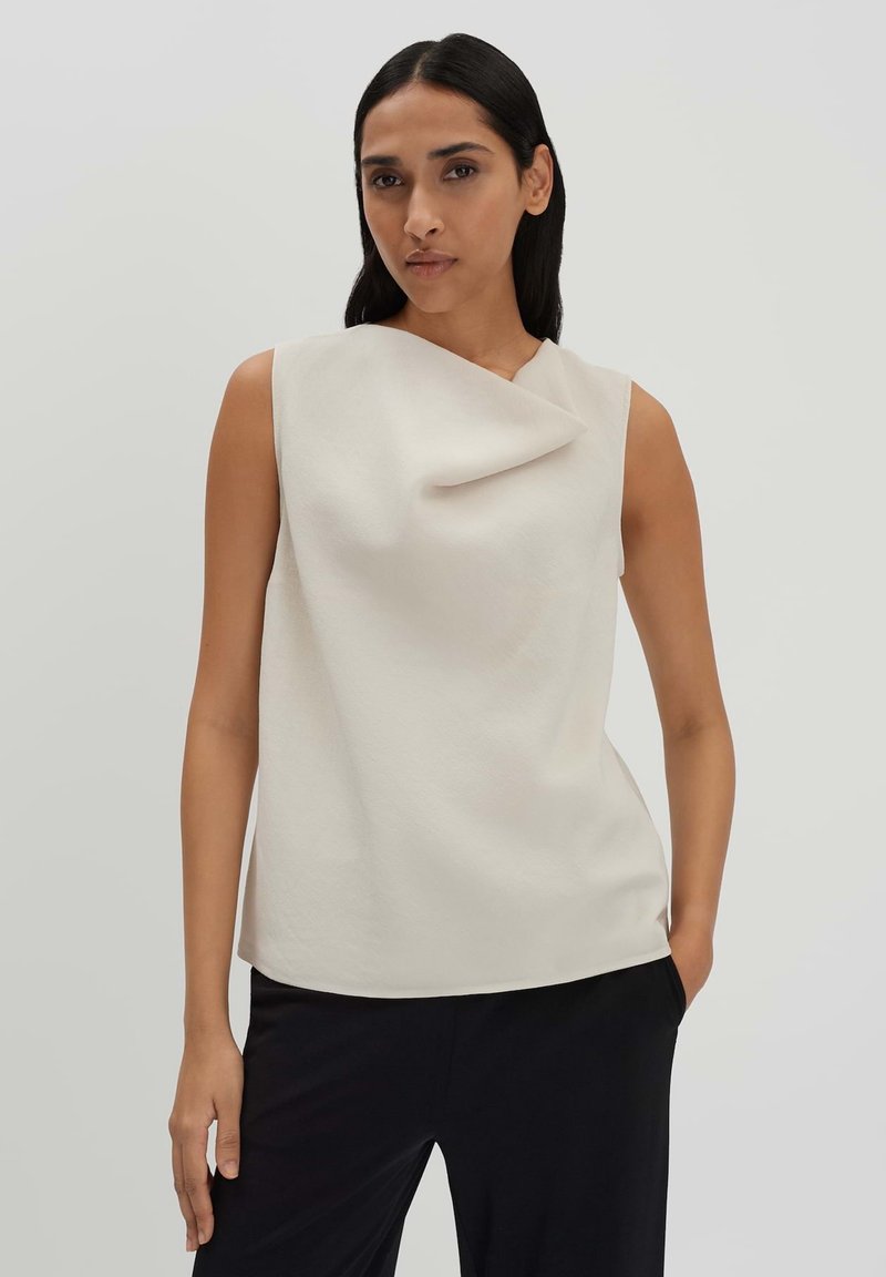 Sleeveless top in soft beige fabric with a draped neckline and smooth texture. Features a relaxed fit and a subtle asymmetrical design.
