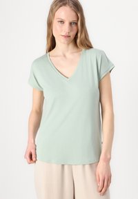 Un tricou V verde mentă fabricat din bumbac moale, cu mâneci scurte răsucite și o croială relaxată, având o textură fină și un design simplu.