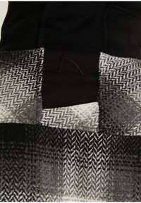 Patchwork de tissu à motif chevron noir et blanc avec un patch central noir arborant un logo discrètement cousu.