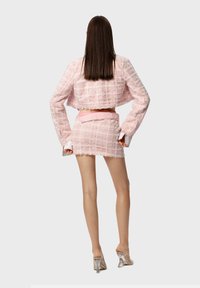 Set di due pezzi in tweed rosa composto da un giacchino corto e una mini gonna, entrambi con un motivo a scacchi testurizzato e bordi sfrangiati.