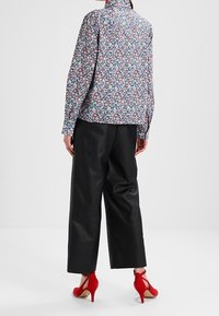 Blouse florale avec un fond sombre, assortie à un pantalon noir large et des chaussures à talons rouges. Tissu lisse et coupe décontractée.