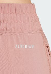 Ružové športové šortky s textúrovanou tkaninou, elastickým pásom a malou zipsovou kapsou. Obsahujú reflexné branding "AEROREADY".