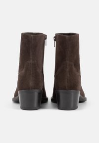 Brown suede ankle boots with a smooth texture, featuring a tapered heel, side zippers, and minimalistic design details.