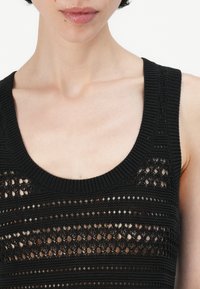 Svart strikket tanktop med rund hals, åpen vev, og brede stropper med ribbet kant.