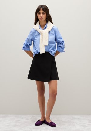 Camicia a righe blu con bottoni, sciarpa in maglia a trecce color crema, gonna nera avvolgente e scarpe ballerine viola. Texture lisce, colori a contrasto e design casual.