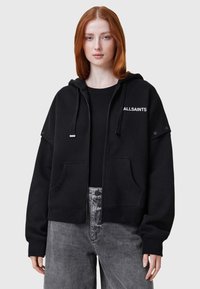 Sudadera negra con capucha y cremallera frontal, grandes bolsillos y el logo "ALLSAINTS" en blanco. Textura suave, corte holgado y detalles de costura.