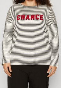 Striped long-sleeve top in cream and navy, featuring a bold red "CHANCE" embroidery across the chest. Soft fabric, relaxed fit.