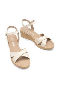 Sandales compensées beige avec brides à la cheville et brides croisées sur fond blanc.