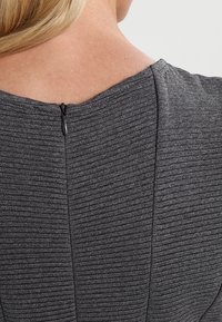 Grå texturerad klänning sedd bakifrån, med horisontella ribbade detaljer och en svart dragkedjestängning vid halsen.