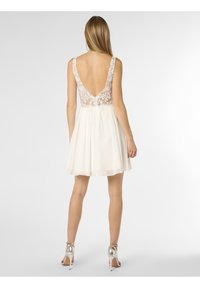 White dress with a lace back, deep V-neckline, and flared chiffon skirt. Paired with silver ankle-strap heels.