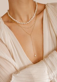 Tres collares de varias capas: uno de perlas blancas, uno de cadena dorada con pequeñas perlas y uno de cadena dorada con un solo colgante de perla.