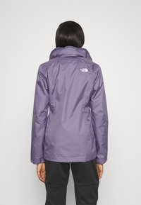 Giacca impermeabile viola con colletto alto e dettaglio logo sul retro. Tessuto liscio e design aderente per l'abbigliamento da esterno.