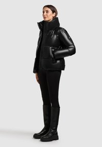 Juodas pūkinis švarkas su aukštu apykakle, blizgiu paviršiumi ir užtrauktuku. Turintis šonines kišenes ir storas, siūdytas dalis. Derinamas su juodomis legginsais ir kelio aukščio botais.