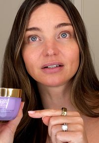 Crème hydratante violette dans un pot en verre avec un couvercle doré, surface lisse et étiquette indiquant "Hydratant Actif Cellules Souches".