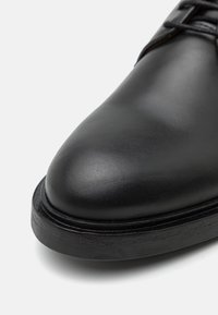 Chaussure noire en cuir avec un bout arrondi, une surface lisse et une épaisse semelle en caoutchouc noire. Présente des coutures discrètes le long du bord.