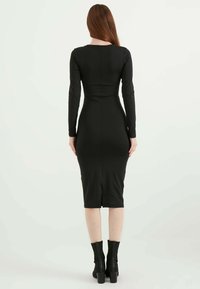 Schwarzes langärmliges Kleid mit taillierter Passform, knielangem Saum und einem Schlitz in der Mitte hinten. Glatte Textur und elegante Silhouette.