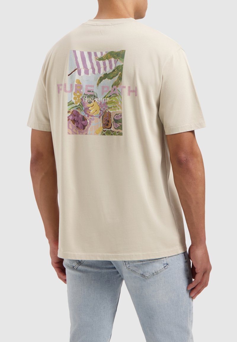 Beige katoenen t-shirt met een kleurrijke fruitmarkt graphic op de achterkant, met de tekst "Pure Path" boven het ontwerp. Korte mouwen, relaxte pasvorm.