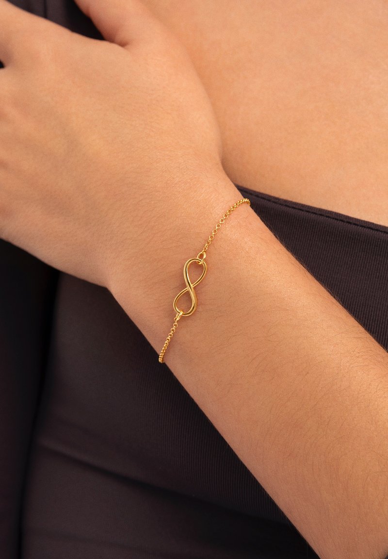 Pulsera de cadena de oro con un símbolo de infinito como elemento principal del diseño, textura suave y un estilo de eslabones delicado.