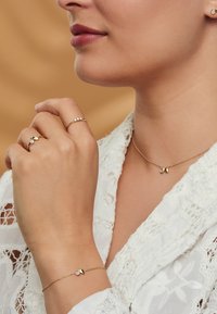 Bijoux en or mettant en valeur un collier délicat avec deux pendentifs, une bague ornée de trois pierres et une bague au design en forme de goutte d'eau, tous portés avec élégance.